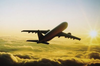 Ein Passagierflugzeug fliegt über den Wolken der Sonne entgegen, die am rechten Bildrand zu sehen ist.